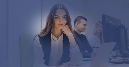 Kvinna vid skrivbord tittar in i kameran och ler