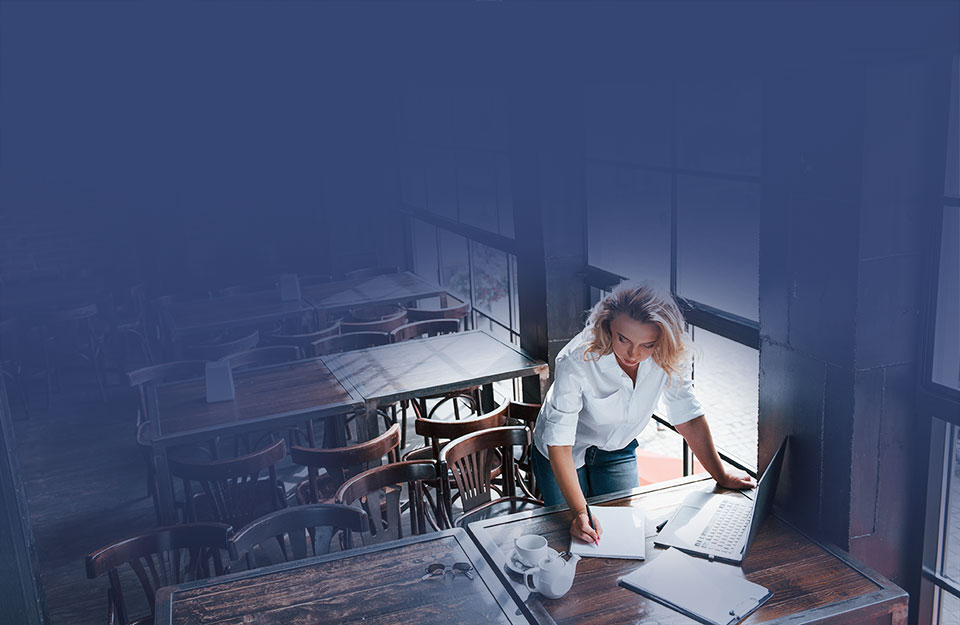 Kvinna står i en tom restaurang och antecknar i ett block på ett bord